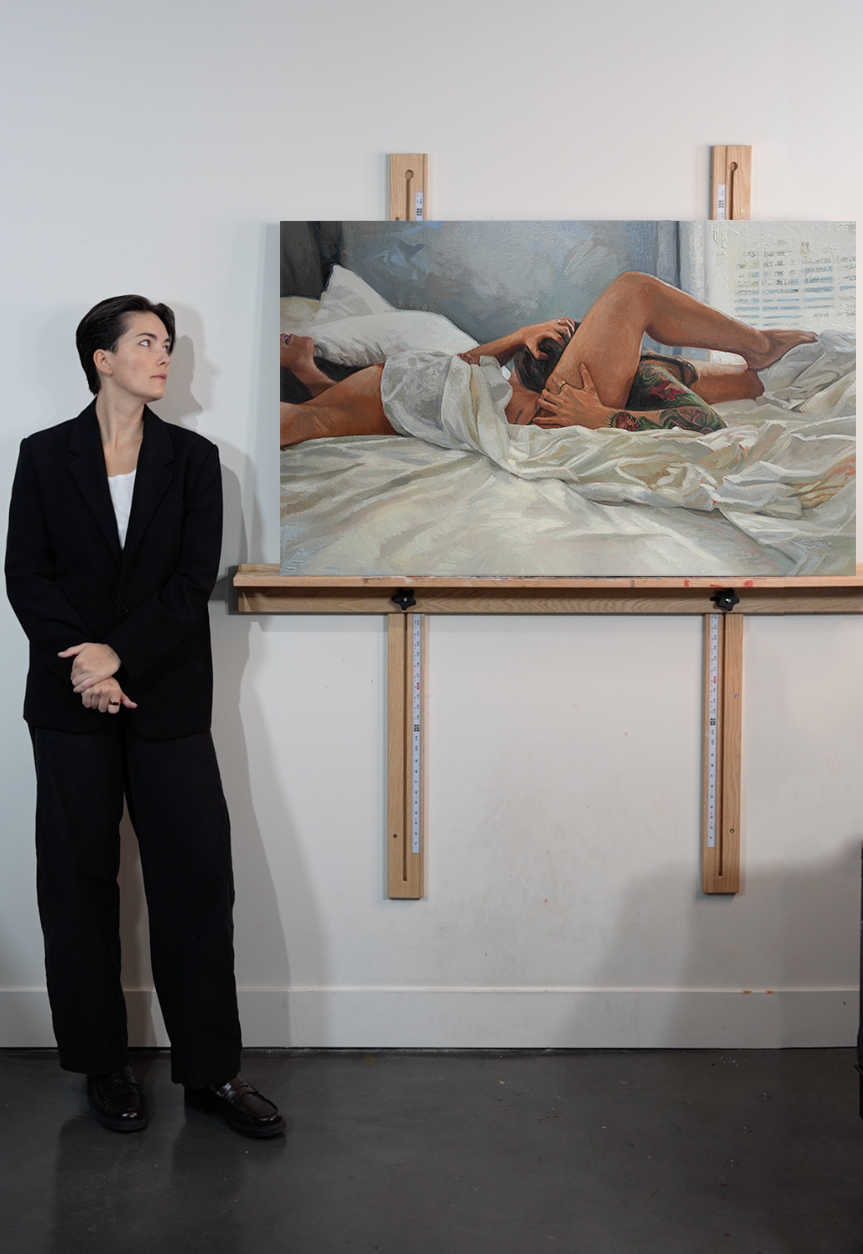 Artist Halie Torris standing in front of her oil painting “Lunch 2.0,” a figurative sapphic artwork exploring intimacy, sensuality, and reclamation.